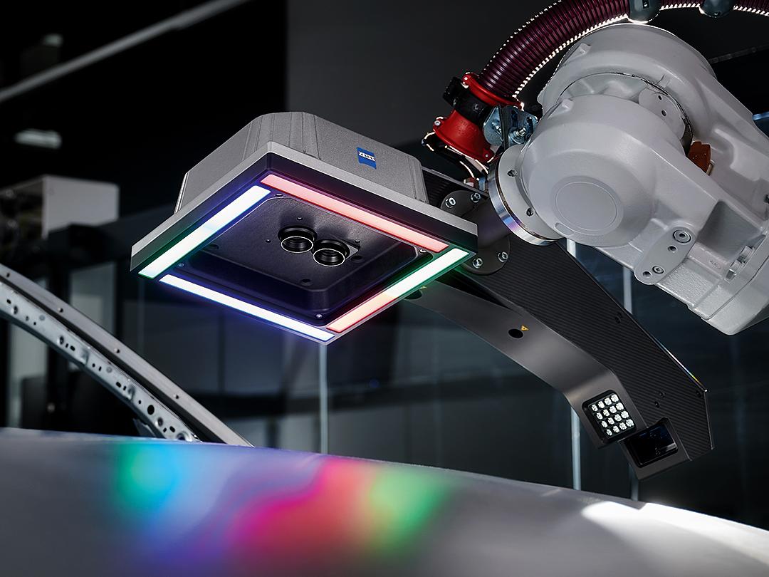 Ramię robota wyposażone w sensor do skanowania 3D ZEISS nad metaliczną powierzchnią, oświetloną wielokolorowymi diodami LED.