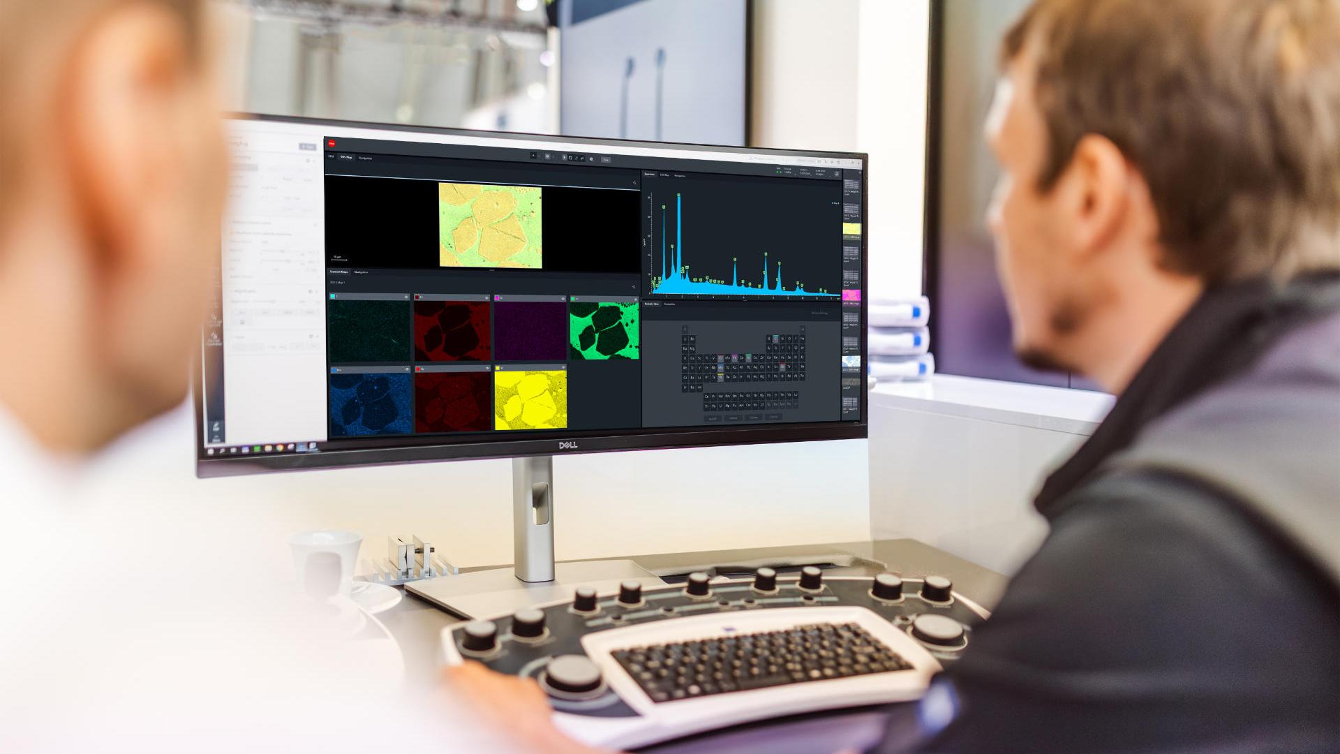 Two people sit in front of a monitor which displays various statistics and other technical diagrams