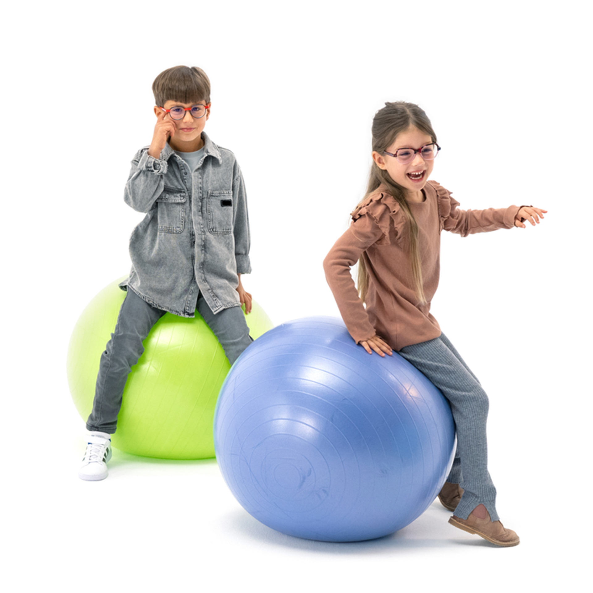 Chłopiec i dziewczynka noszący okulary skaczą radośnie na piłkach gimnastycznych.