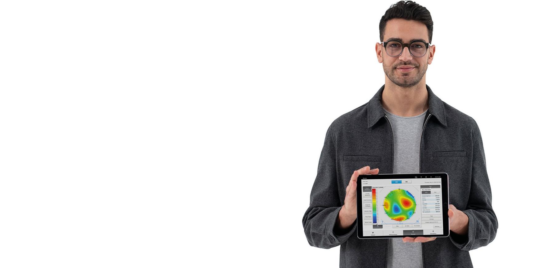 Młody mężczyzna w okularach z soczewkami ZEISS spogląda prosto w kamerę i trzyma iPada, na którym widać wstępne informacje bazowe niezbędne do dokładnej subiektywnej refrakcji.
