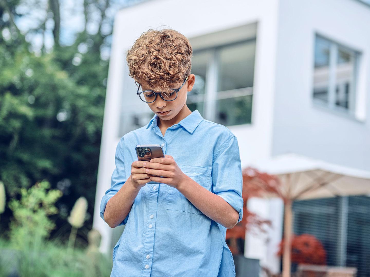 Młody chłopiec przebywa na zewnątrz i patrzy w telefon.