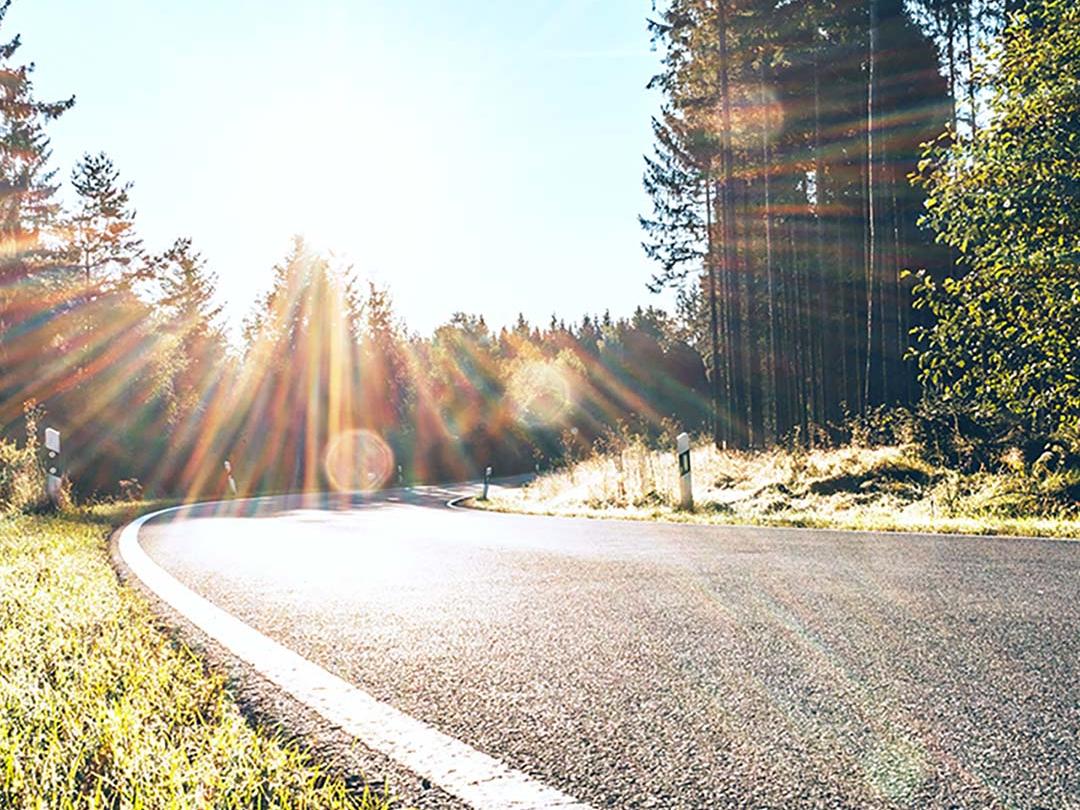 Obraz z suwakiem, na którym jedna połowa przedstawia drogę w lesie z intensywnym światłem słonecznym, a druga tę samą drogę z redukcją odblasków i zwiększonym kontrastem, podkreślając efekt polaryzacyjnych soczewek okularów przeciwsłonecznych.