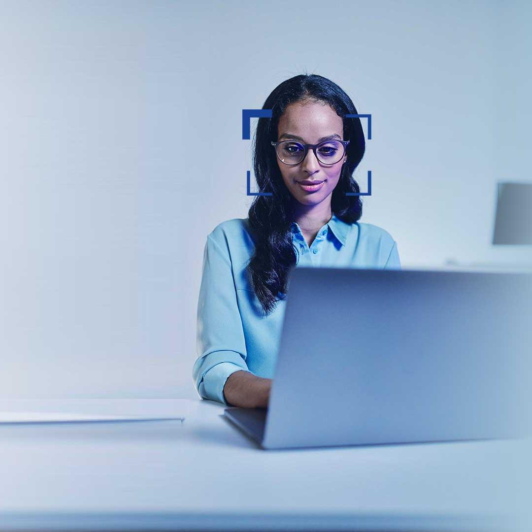 Kobieta z czarnymi włosami, w okularach, patrzy uśmiechnięta w ekran laptopa