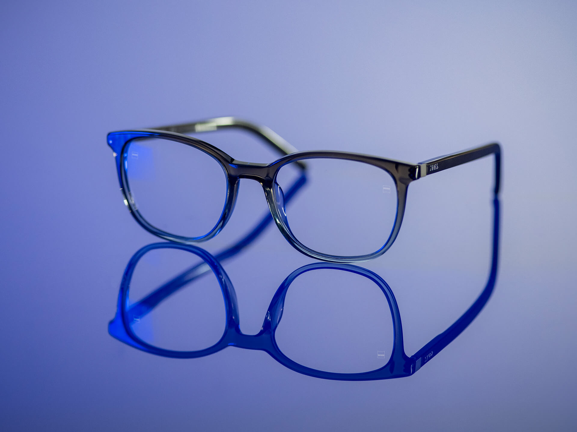 Okulary widziane w niebieskawym świetle z soczewkami ZEISS z materiałem soczewkowym BlueGuard. Jedynie niewielkie niebieskie odblaski są widoczne na powierzchni soczewek.
