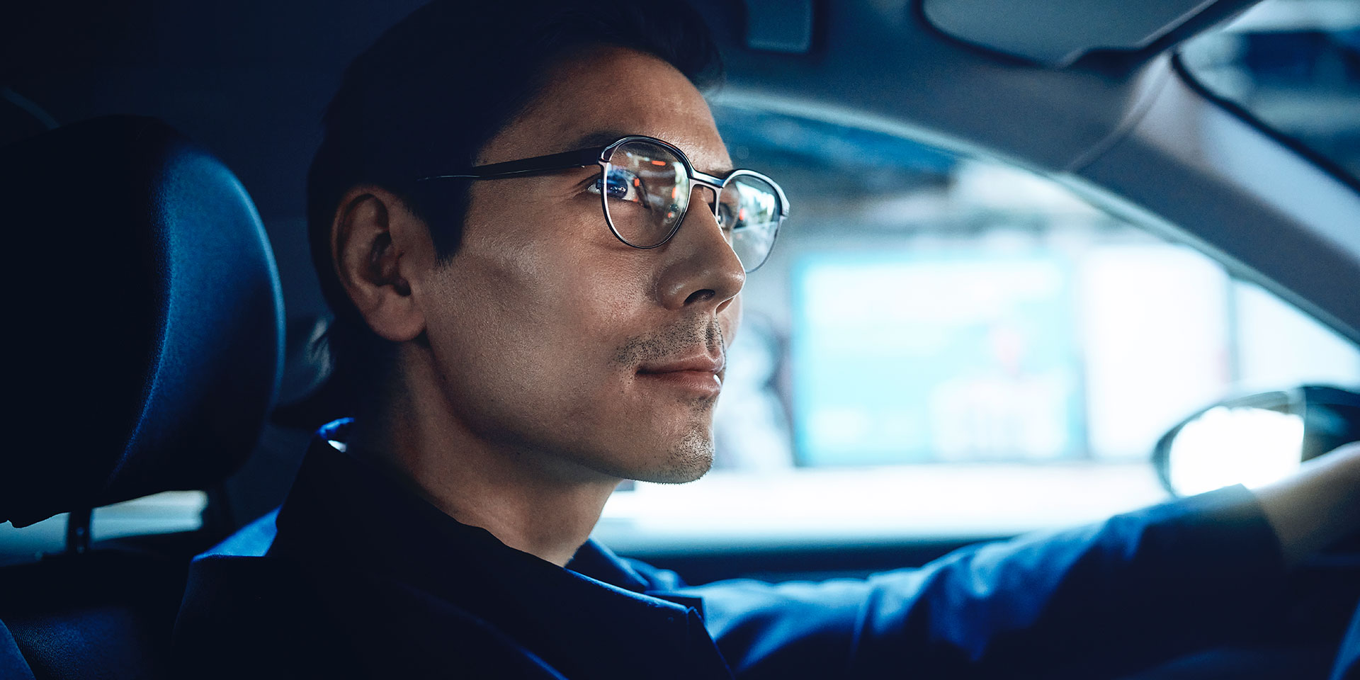Mężczyzna prowadzący samochód, wyglądający na pewnego siebie z lekkim uśmiechem. Mężczyzna nosi soczewki jednoogniskowe ZEISS DriveSafe.