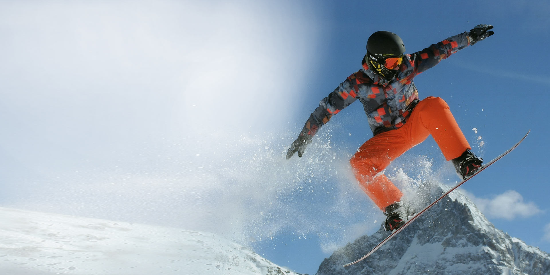 Mężczyzna skaczący na desce snowboardowej, noszący czarny kask narciarski i gogle narciarskie ZEISS z technologią Interchangeable zapewniającą ochronę