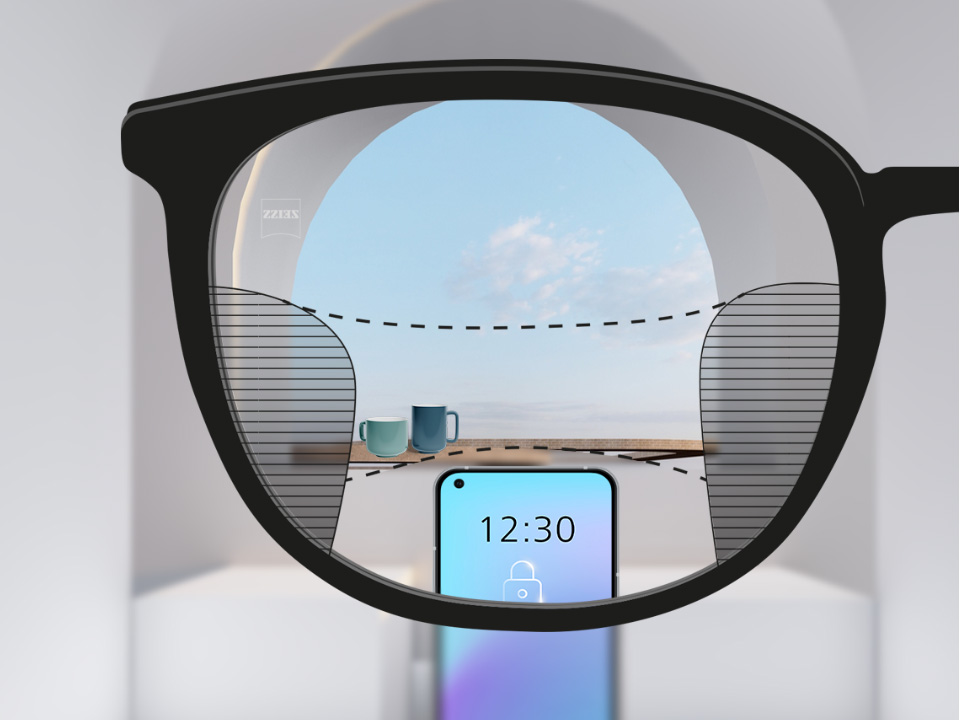 Punkt widzenia z soczewkami progresywnymi ZEISS SmartLife ze smartfonem i kubkami w tle, obraz widziany przez soczewkę jest w pełni wyraźny, po bokach widoczne delikatne rozmycie.