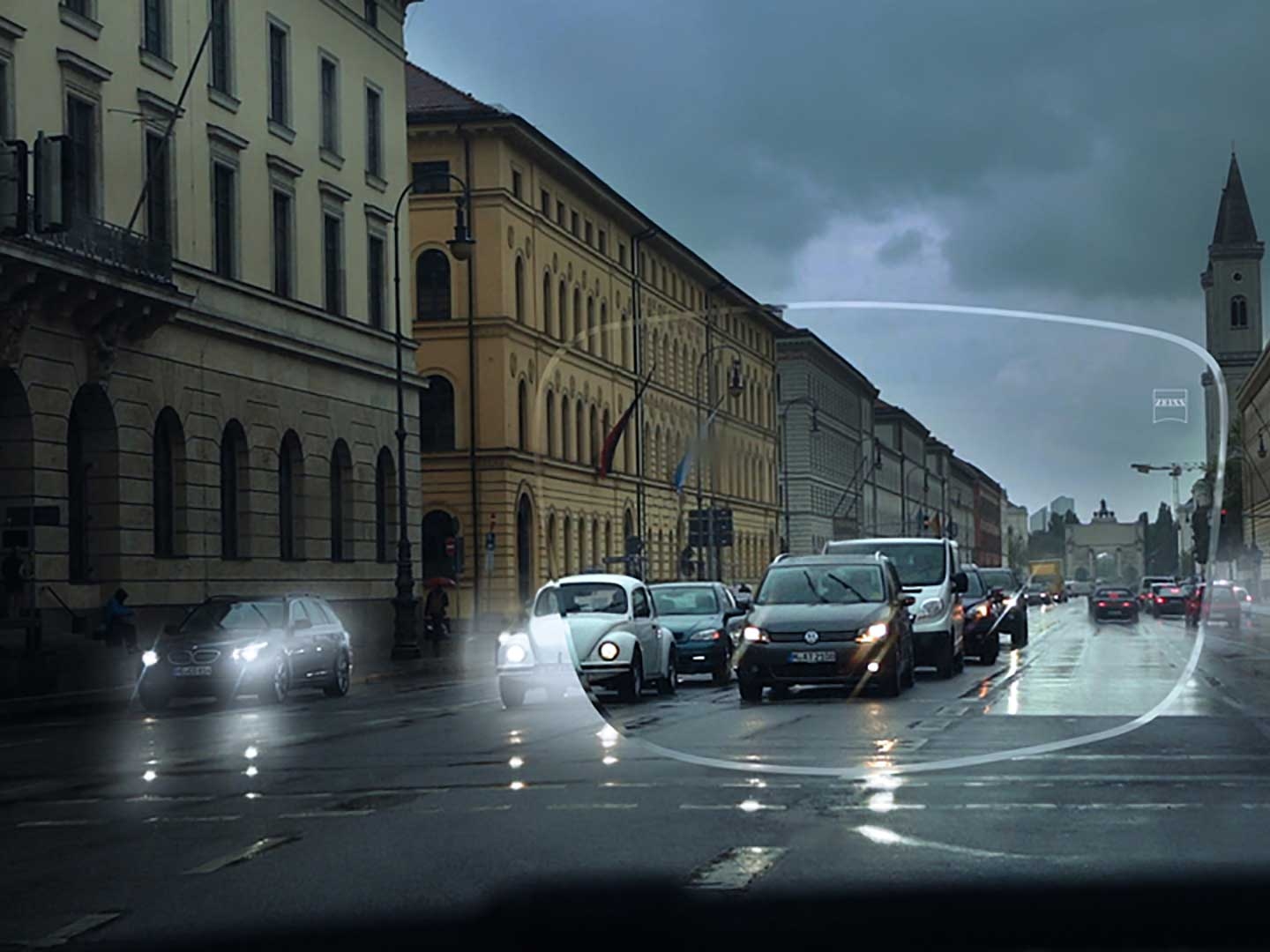 Obraz ilustruje słabą widoczność w warunkach niedostatecznego oświetlenia na ulicy. Punktem widzenia jest wnętrze samochodu widziane przez soczewkę okularową. 