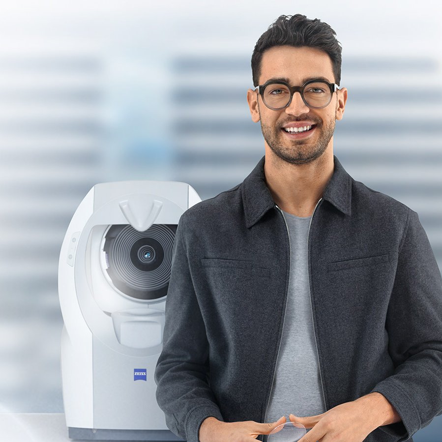 Krótko ostrzyżony młody brunet w okularach z soczewkami ZEISS, uśmiechający się do kamery. W tle widoczny  ZEISS i.Profiler plus.